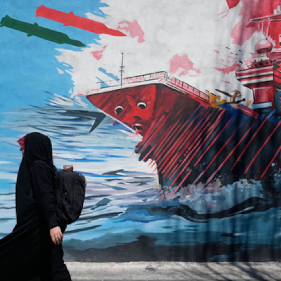 Una mujer pasa junto a un mural que muestra un portaaviones estadounidense bajo ataque en el centro de Teherán.