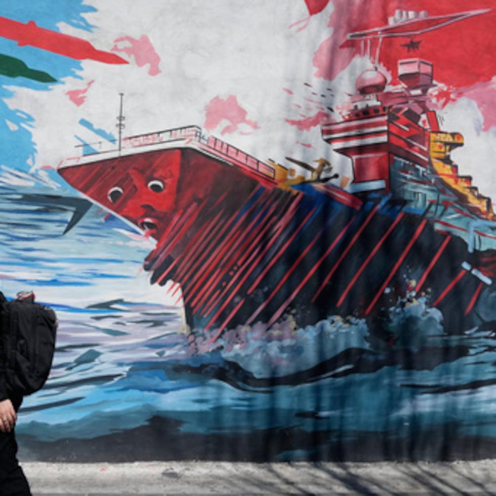 Una mujer pasa junto a un mural que muestra un portaaviones estadounidense bajo ataque en el centro de Teherán, Irán.