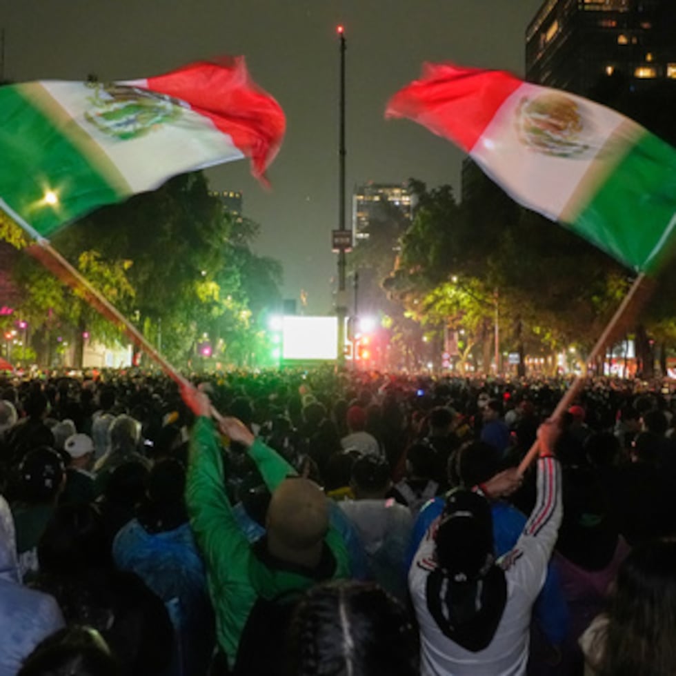 Los aficionados mexicanos agitan banderas mientras ven el partido de la ronda de 32 de la Copa del Mundo entre México y Ecuador, cerca del monumento al Ángel de la Independencia en Ciudad de México.
