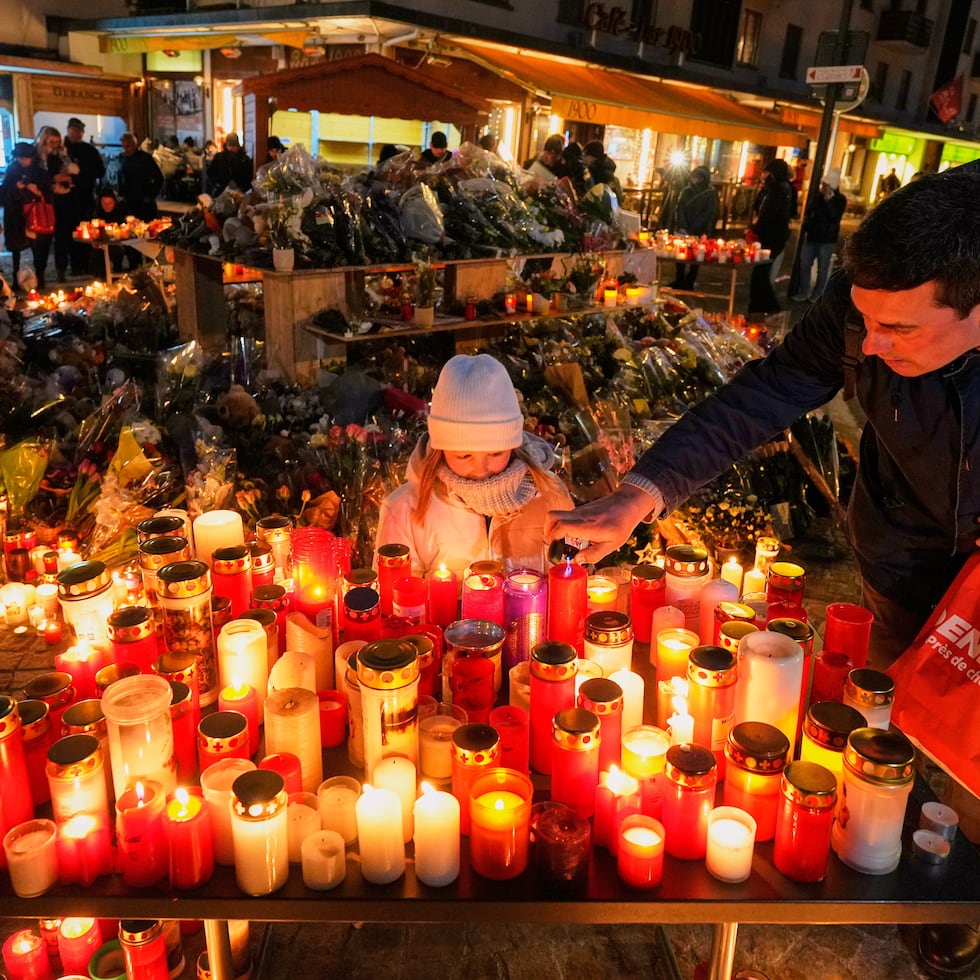 Una niña observa mientras un adulto coloca una vela en el exterior del bar Le Constellation, en Crans-Montana, en los Alpes suizos.