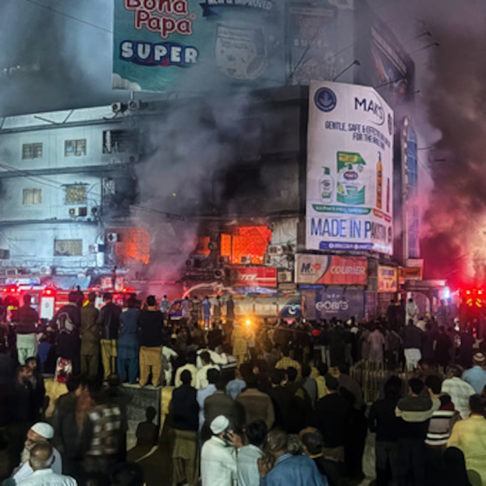 Gente reunida mientras los bomberos intentan controlar un enorme incendio en un centro comercial.