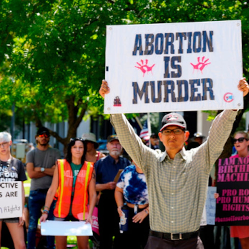 Un hombre que apoya las restricciones al aborto sostiene un cartel mientras partidarios del derecho al aborto sostienen carteles detrás de él frente al Capitolio Estatal de Carolina del Sur el jueves, 7 de julio de 2022, en Columbia, Carolina del Sur.