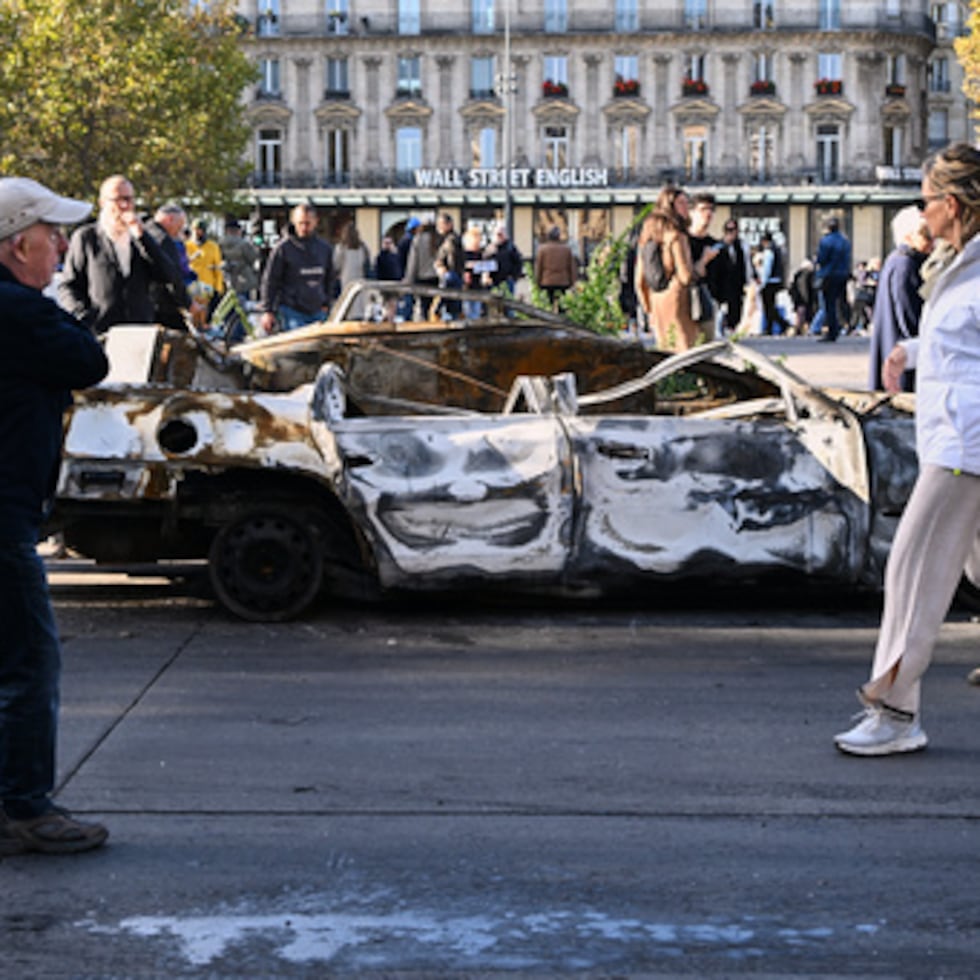 Varias personas observan un coche calcinado en la Place de la République al día siguiente de una manifestación contra el aumento del costo de la vida, en la que se sumaron las reivindicaciones de los estudiantes, en París, el domingo 18 de octubre de 2026.