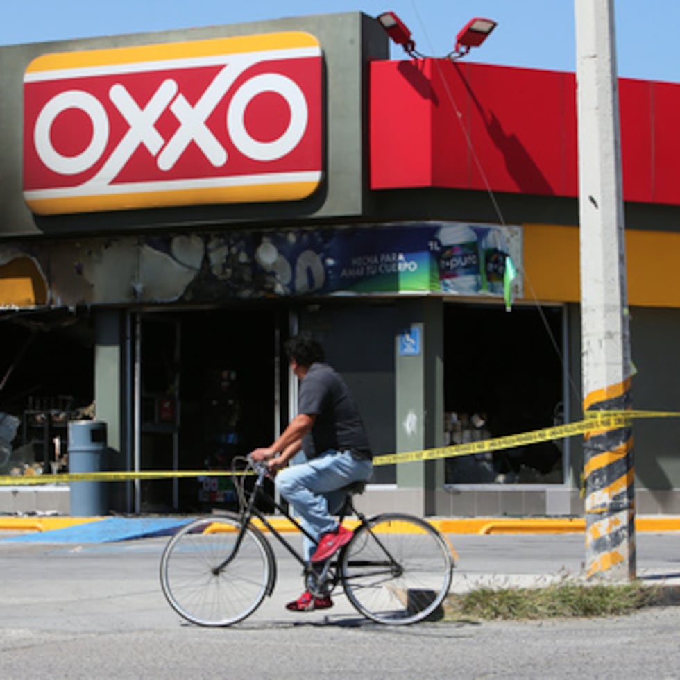 Un hombre anda en bicicleta junto a una tienda de conveniencia incendiada el domingo en San Francisco del Rincón, Guanajuato.