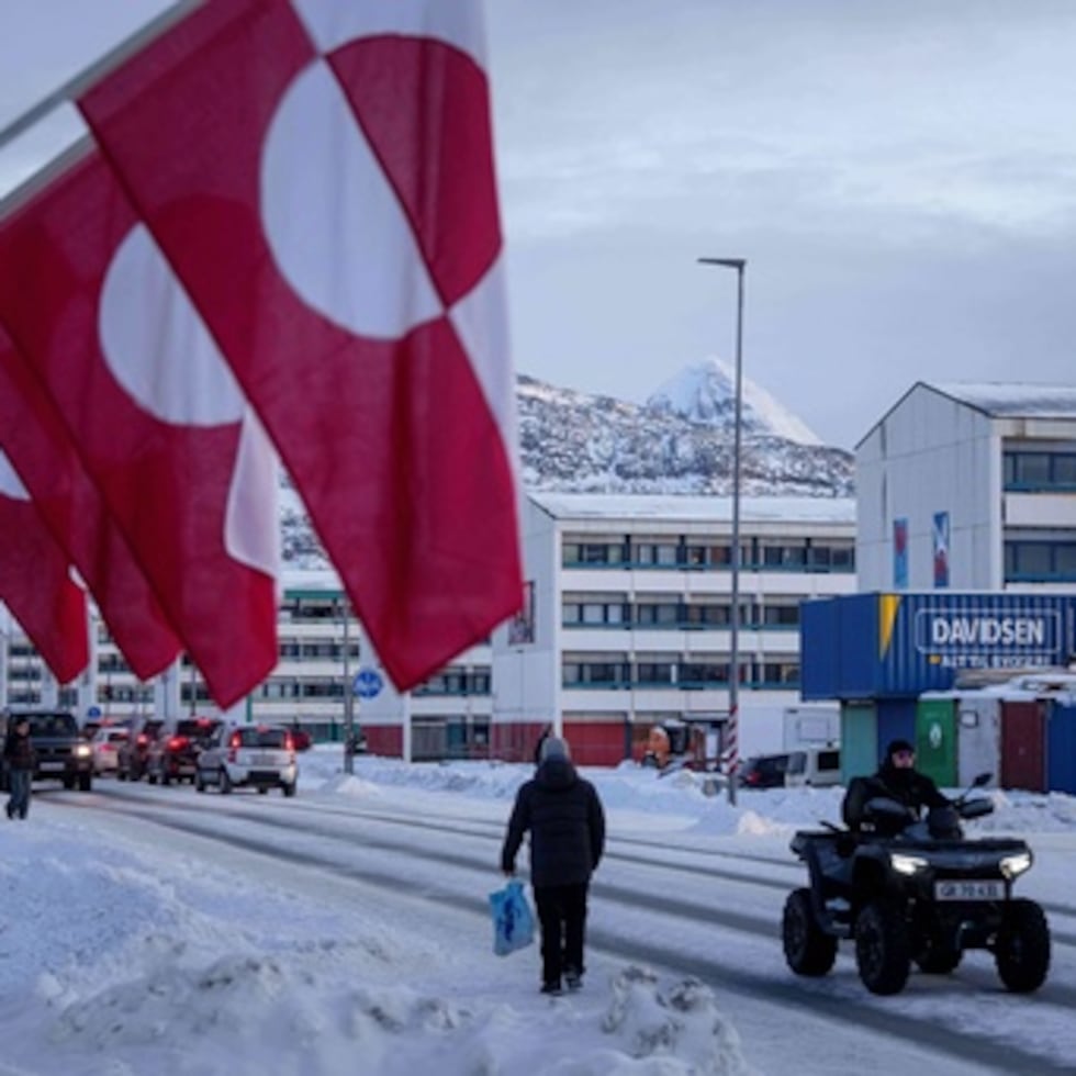 Un hombre pasa en quad junto a una hilera de banderas nacionales de Groenlandia en Nuuk, Groenlandia, miércoles 14 de enero de 2026. (AP Photo/Evgeniy Maloletka)