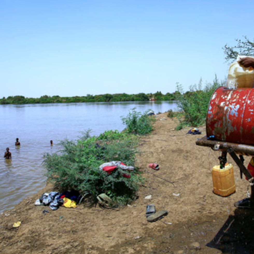 La escasez de agua en Jartum, Sudán, obliga a los residentes a buscar alternativas. Niños se bañan en el Nilo mientras un hombre llena un contenedor.