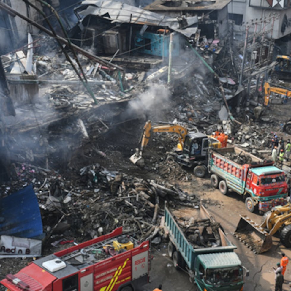 Rescatistas y bomberos trabajan con maquinaria pesada para buscar entre los escombros tras un incendio masivo en Karachi.