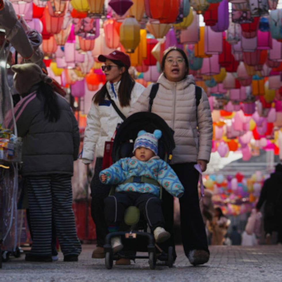 ARCHIVO - Unas mujeres empujan a un niño pequeño en un cochecito mientras recorren la calle comercial Qianmen, decorada con farolillos, en Pekín, China, el 12 de enero de 2026. (AP Photo/Andy Wong, Archivo)
