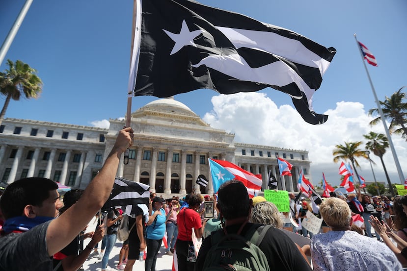 Un manifestante ondea una bandera de Puerto Rico en blanco y negro frente al Capitolio antes del inicio de la marcha convocada por los cantantes Bad Bunny, Ricky Martin, Ednita Nazario y René Pérez, entre otros.