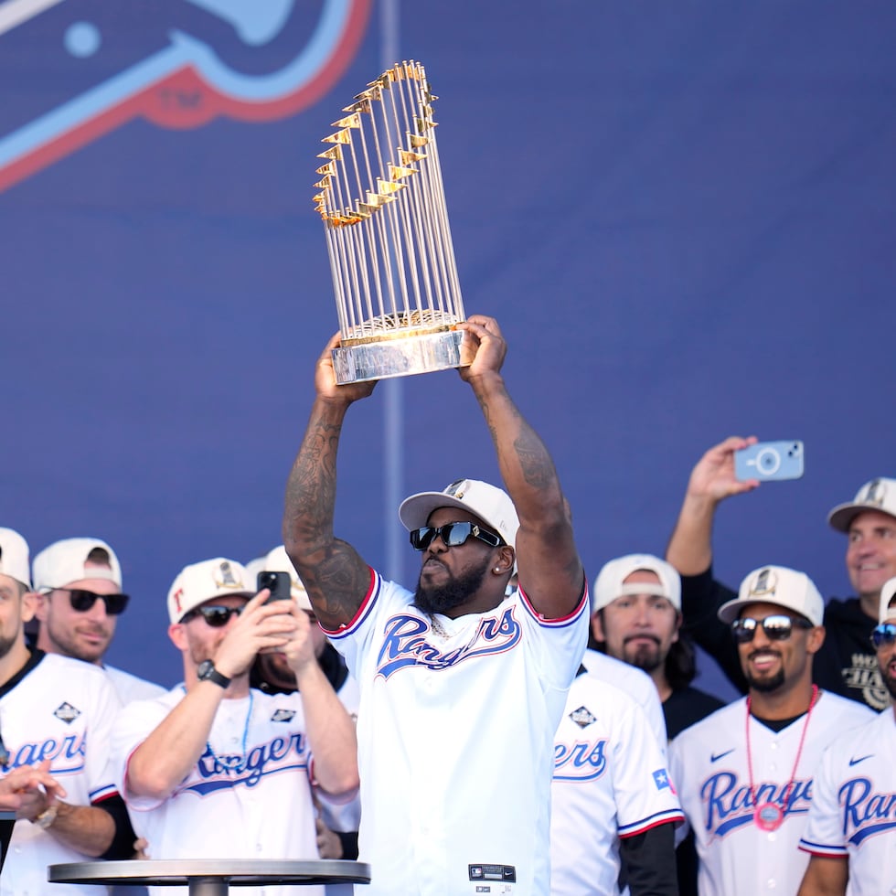 Adolis García, sosteniendo en alto el trofeo de campeonato de la Serie Mundial de 2023, rodeado por compañeros de los Rangers.