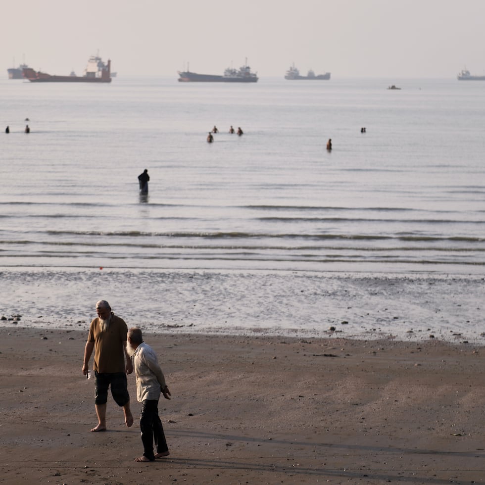 Personas caminan por la playa mientras otras se adentran en el agua en el estrecho de Ormuz.