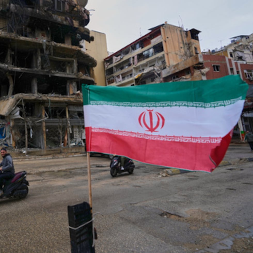 Un hombre en motoneta pasa cerca de una bandera iraní colocada frente a un edificio destruido tras un cese el fuego entre Hezbolá e Israel, en Dahiyeh, en los suburbios del sur de Beirut, Líbano, el lunes 20 de abril de 2026. (AP Foto/Hussein Malla)