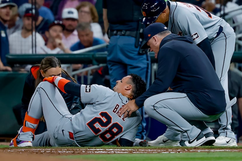 El jugador de los Tigers, Javier Báez (28), es examinado por el dirigente de los Tigers, A. J. Hinch, a la derecha, y un miembro del equipo médico tras lesionarse la pierna derecha al correr hacia la primera base.