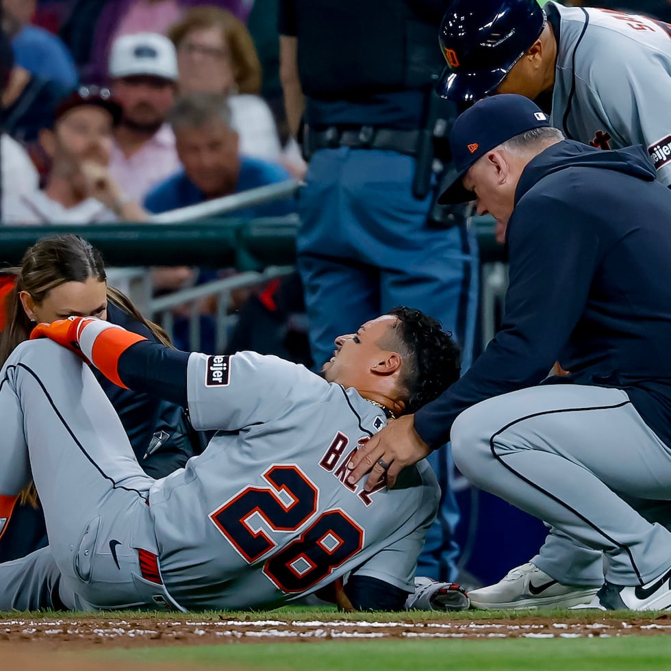 El jugador de los Tigers, Javier Báez (28), es examinado por el dirigente de los Tigers, A. J. Hinch, a la derecha, y un miembro del equipo médico tras lesionarse la pierna derecha al correr hacia la primera base.