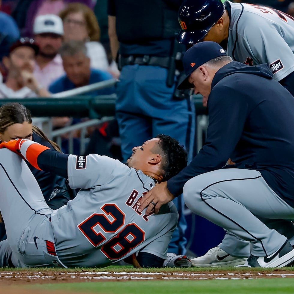El jugador de los Tigers, Javier Báez (28), es examinado por el dirigente de los Tigers, A. J. Hinch, a la derecha, y un miembro del equipo médico tras lesionarse la pierna derecha al correr hacia la primera base el 29 de abril.