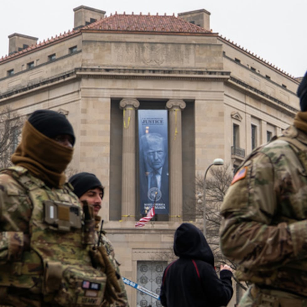 Miembros de la Guardia Nacional pasan junto a una pancarta con el presidente Donald Trump colgada en el Departamento de Justicia, el jueves 19 de febrero de 2026, en Washington.