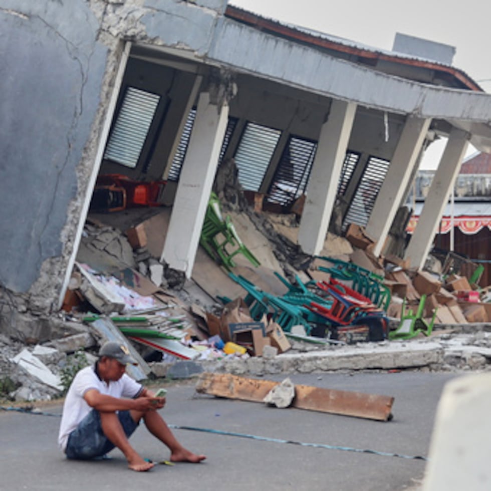 Un hombre consulta su móvil cerca de un edificio derrumbado a causa de un terremoto, en Reok, provincia de Nusa Tenggara Oriental, Indonesia.