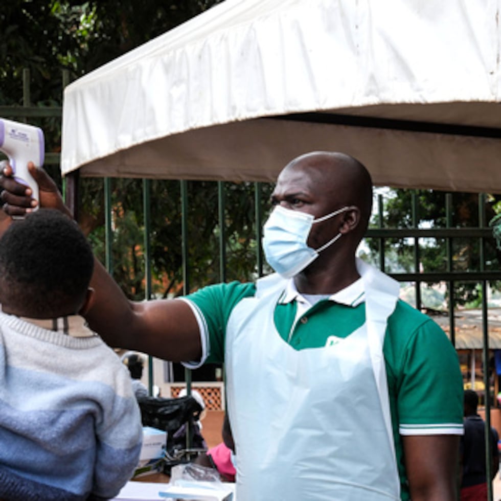 Un funcionario de salud utiliza un termómetro para examinar a la gente frente al Hospital Musulmán Kibuli en Kampala, Uganda, sábado, 16 de mayo.
