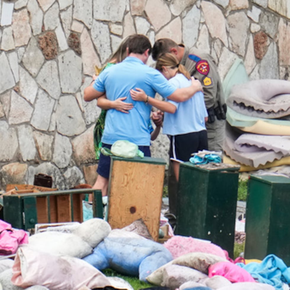 FILE - An officer prays with a family as they pick up items at Camp Mystic in Hunt, Texas, July 9, 2025. (AP Photo/Ashley Landis, File)