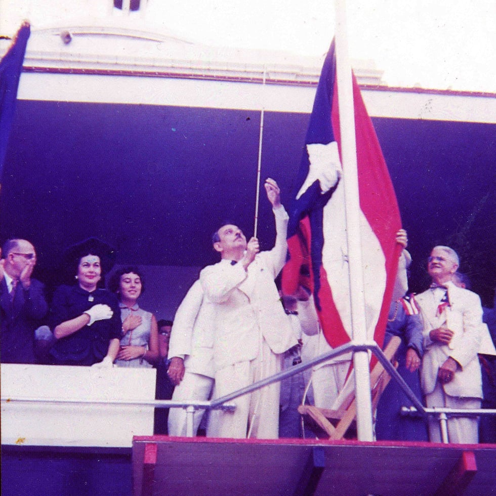 Constitución del Estado Libre Asociado de Puerto Rico: Luis Muñoz Marín iza la bandera de Puerto Rico acompañado por funcionarios del gobierno y por su familia.