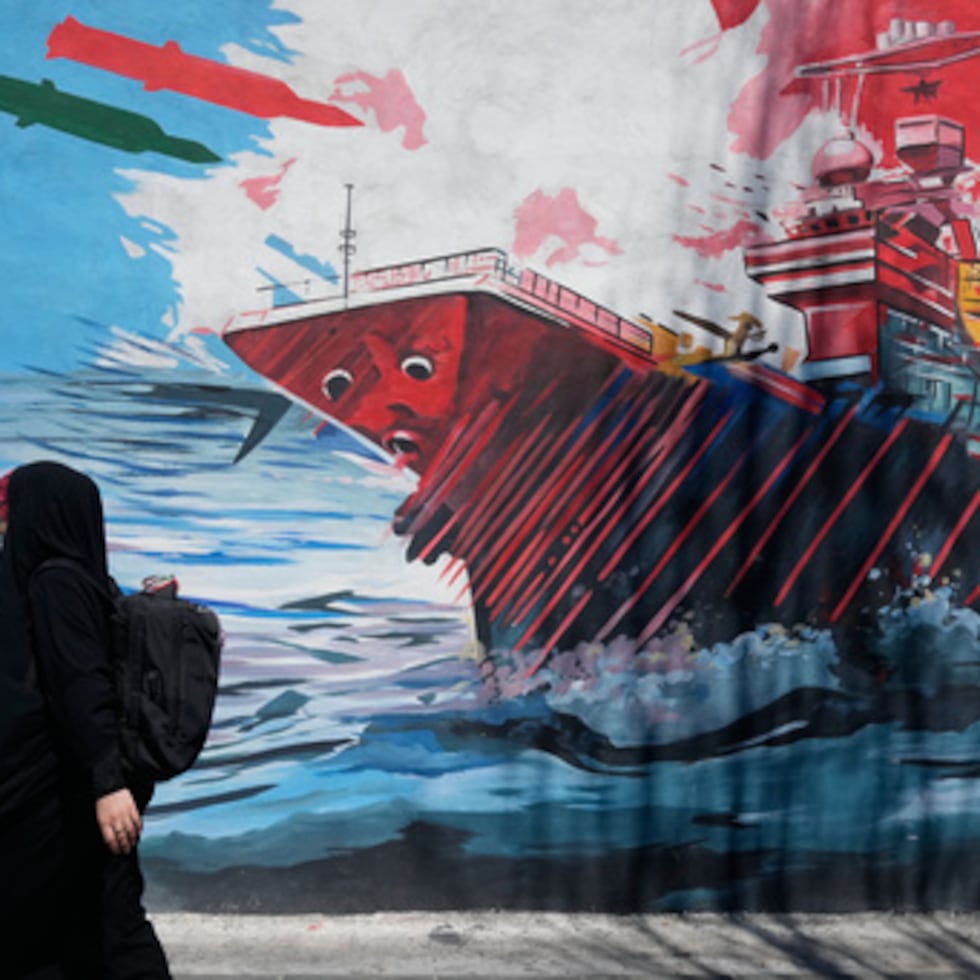 Una mujer pasa junto a un mural que representa un portaaviones estadounidense bajo ataque con misiles en el centro de Teherán, Irán,