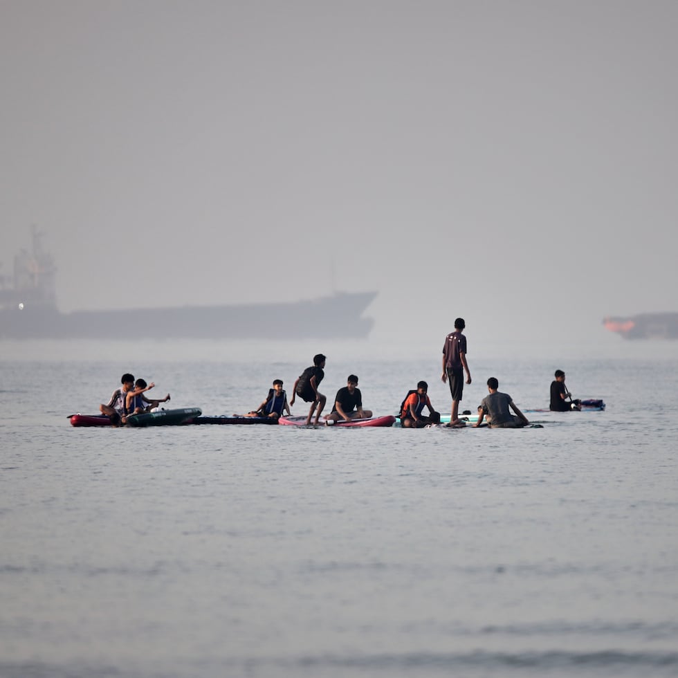 Varias personas se congregan en tablas de remo en aguas poco profundas al tiempo que buques de carga y de servicio permanecen anclados en el estrecho de Ormuz, frente a Bandar Abbas, Irán, el lunes 1 de junio de 2026. (Amirhosein Khorgooi/ISNA vía AP)