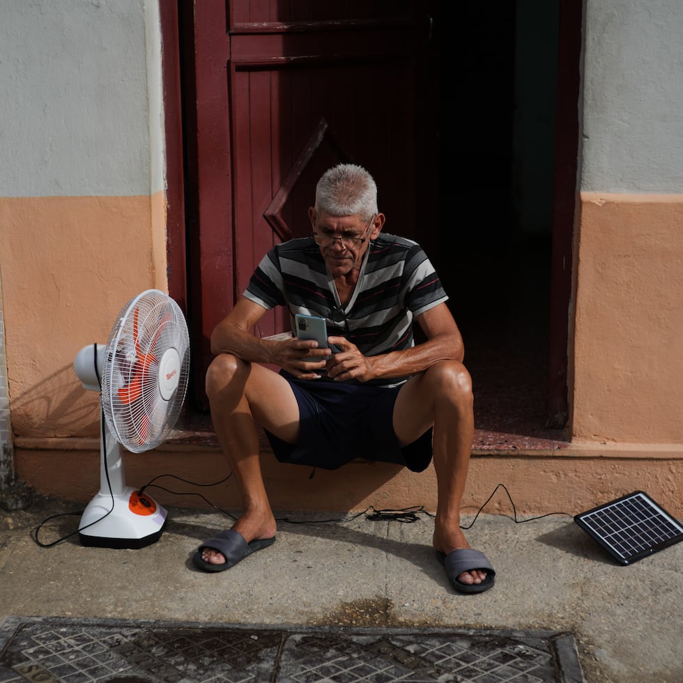 Un hombre carga su ventilador y su teléfono celular con un panel solar durante un apagón en La Habana.