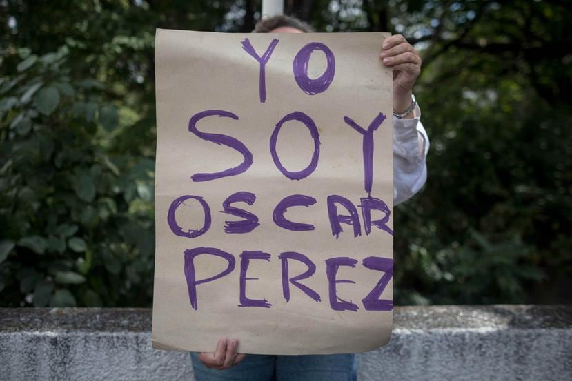 Una mujer sostiene un cartel en el que se lee "Yo soy Óscar Pérez" frente a miembros de la Guardia Nacional Bolivariana y la Policía Nacional Bolivariana que custodian las inmediaciones de la morgue en donde está cuerpo del exagente Pérez, en Caracas, Ven