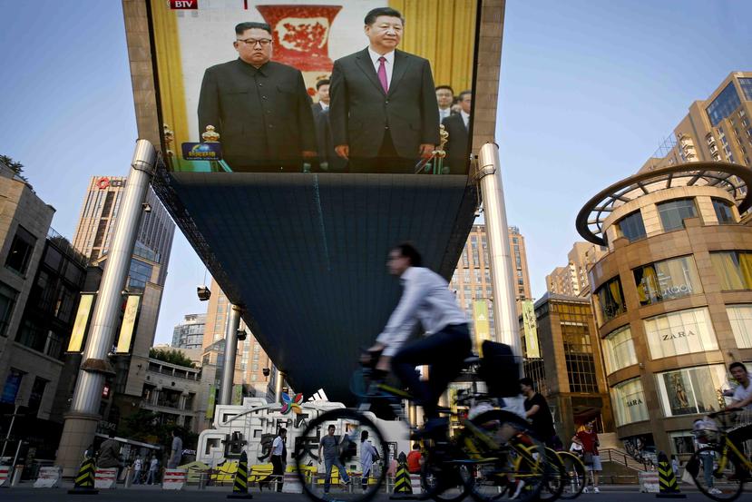 Gente pasa frente a una pantalla gigante que transmite la reunión del líder norcoreano Kim Jong Un con el presidente chino Xi Jinping. (AP)