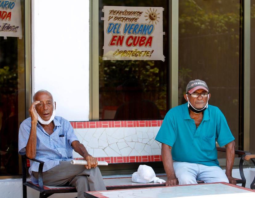 Dos hombres con la mascarilla mal puesta descansan fuera de una cafetería este martes, en La Habana, (Cuba).