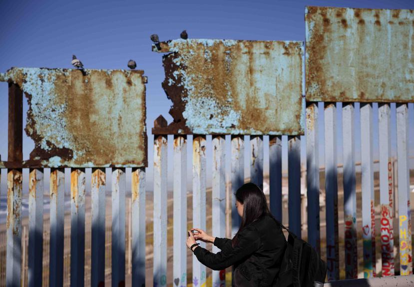 Una mujer toma fotos de un tramo herrumbrado del muro fronterizo entre EEUU y México cerca de Tijuana, México. (AP)