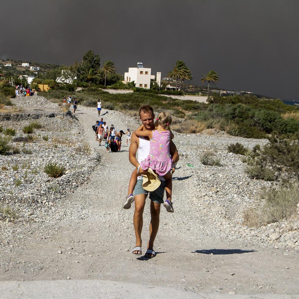 Un hombre carga a una niña al abandonar la zona donde arde un incendio forestal en la isla de Rodas, Grecia.