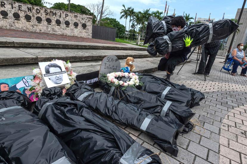 Una persona pone en el suelo unas bolsas con supuestos "cadáveres" que representan a los muertos por coronavirus este miércoles durante la protesta contra la reapertura de la economía en el parque de la Antorcha de la Amistad en el centro de Miami. (Agenc