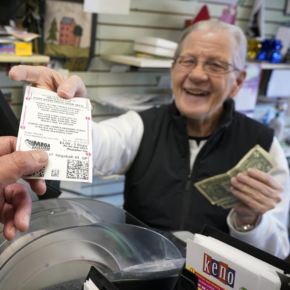 En esta imagen de archivo, Dot Skoko, propietario de la tienda Dot's Dollar More or Less en Mt. Lebanon, Pensilvania, entrega un boleto de la lotería Mega Millions a un cliente