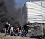 Manifestantes palestinos se guarecen durante enfrentamientos con fuerzas israelíes el viernes 14 de mayo de 2021 en el retén de Hawara, al sur de la ciudad cisjordana de Nablus. (AP Foto/Majdi Mohammed)