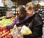 Catherine Langabeer, izquierda, jefa de sostenibilidad de la cadena de supermercado Countdown, y la ministra de Medio Ambiente, Rachel Brooking, muestran cómo utilizar una bolsa de poliester reutilizable, el 29 de junio de 2023, en Wellington, Nueva Zelanda.