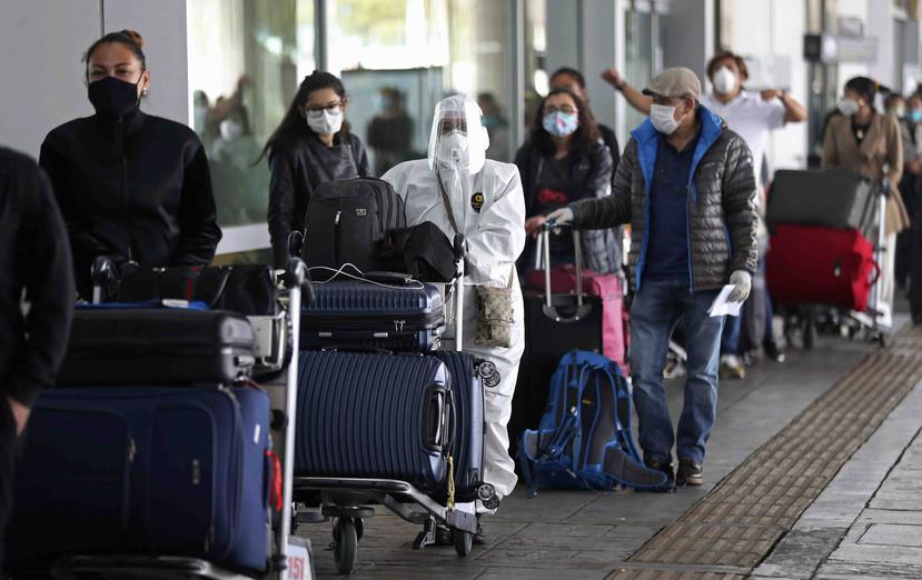 Pasajeros están formados para un vuelo humanitario a Italia usando equipo de protección por la pandemia del nuevo coronavirus, lo que ha ocasionado la cancelación de vuelos nacionales e internacionales en el aeropuerto El Dorado en Bogotá, Colombia. (AP)