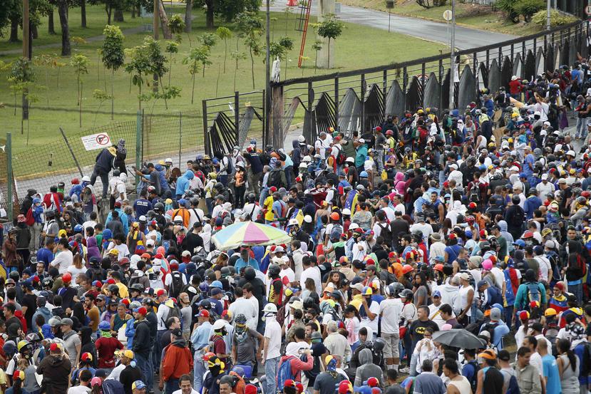 Manifestantes protestan al frente de la verja de la base aérea La Carlota durante una protesta en la autopista Francisco Fajardo. (AP)