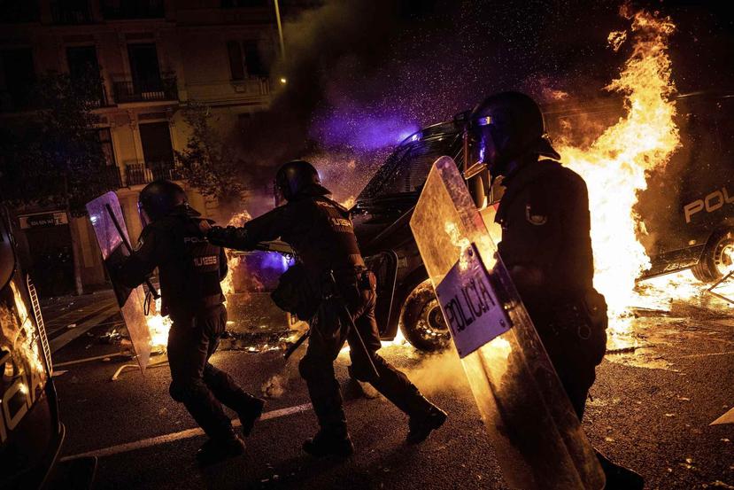 Agentes de policía corren mientras una de sus camionetas cruza una barricada en llamas durante enfrentamientos entre manifestantes y policías en Barcelona. (AP)