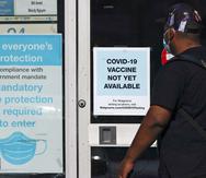 Un individuo pasa junto a una tienda de Walgreens que tiene un cartel que dice que todavia no hay disponible una vacuna contra el COVID-19.