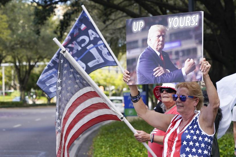 Seguidores de Donald Trump ondean banderas y letreros a los conductores que pasan frente al centro de convenciones en la Conferencia de Acción Política Conservadora.