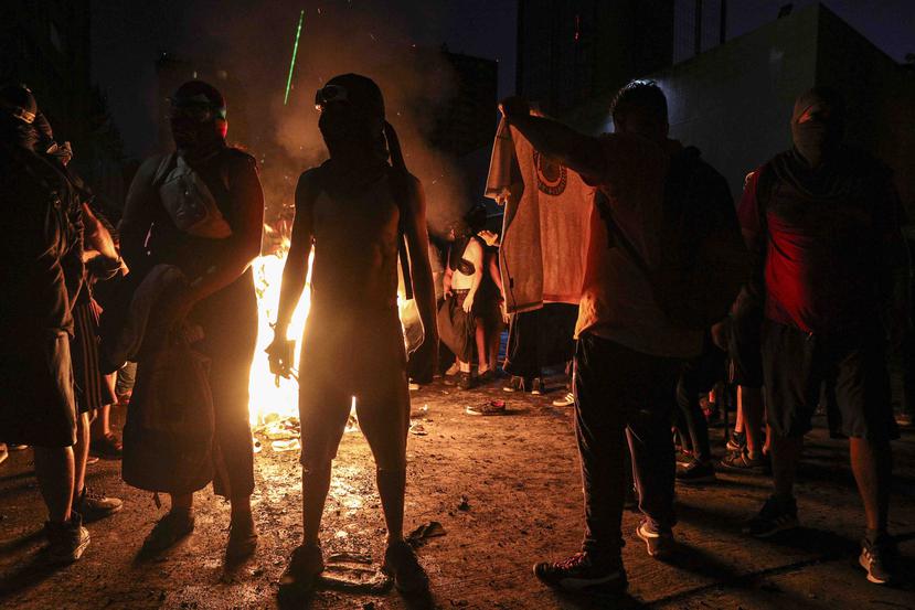 Manifestantes contra el gobierno empapados por un cañón hidrante de la policía se secan junto a una barricada en llamas en Santiago de Chile. (AP)
