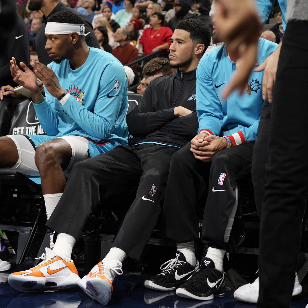 Devin Booker, base de Suns de Phoenix, de negro, está sentado en la banca, al lado de Torrey Craig en la primera mitad del juego de baloncesto de la NBA en contra de los Nuggets de Denver, el domingo 25 de diciembre de 2022, en Denver.