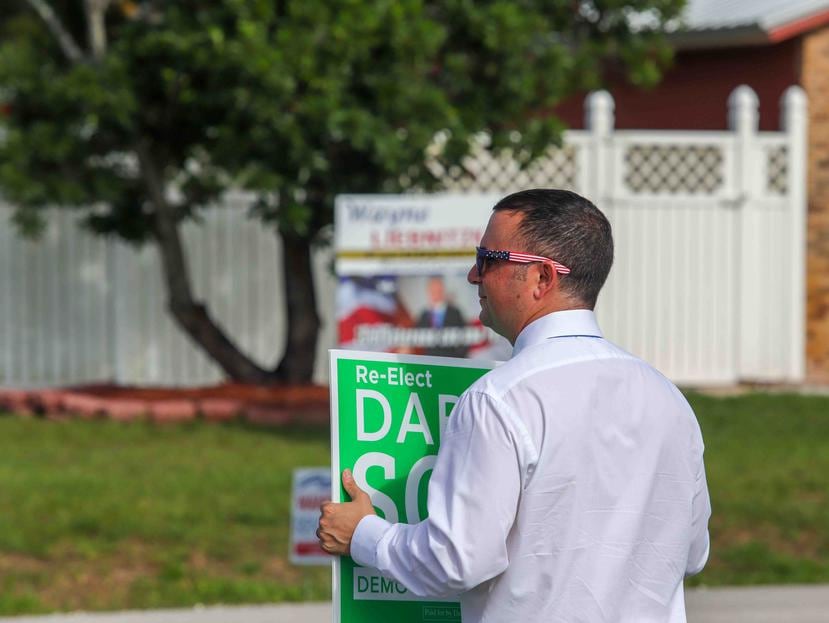 Darren Soto sujetando un rótulo color verde y blanco con su nombre en letras grandes frente al centro de votación Roberto Guevara.