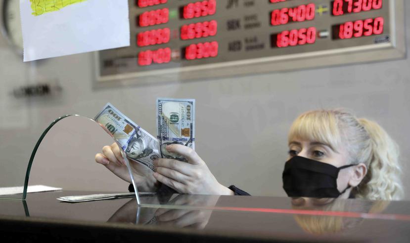 Una empleada con mascarilla sanitaria cambia liras turcas por dólares estadounidenses en una casa de cambio en Ankara, Turquía. (AP)