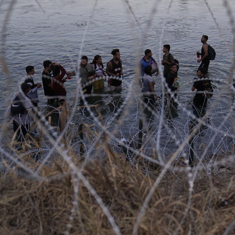 Migrantes esperan para trepar por encima del alambre de púas después de cruzar el Río Bravo y entrar en Estados Unidos desde México.
