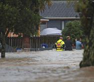 Personal de emergencia y un hombre atraviesan las aguas de una inundación en Auckland, Nueva Zelanda.