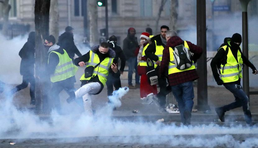 Un manifestante con un chaleco amarillo patea una lata de gas lacrimógeno durante una manifestación en París (AP)