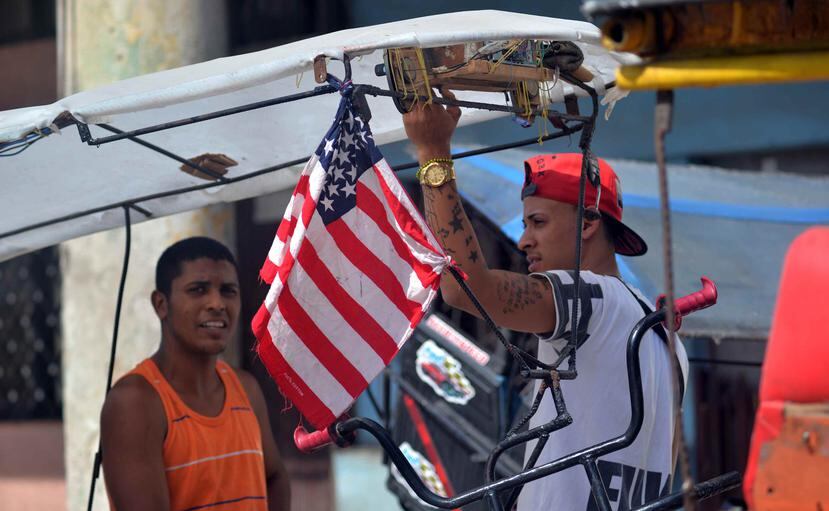 Dos bicitaxistas conversan junto a una bandera de Estados Unidos por una calle de La Habana (Cuba), pocos días antes de la llegada del presidente Barack Obama, a la isla. (EFE / Rolando Pujol)